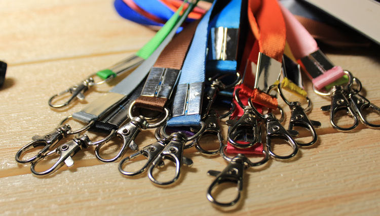 Assorted colors of custom nylon lanyards with metal lobster clips displayed on wooden surface