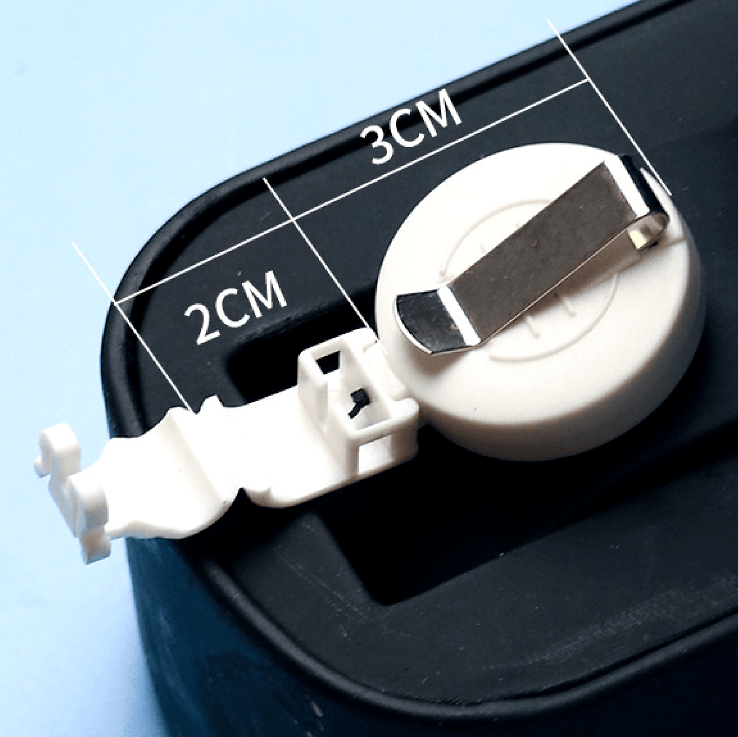 Close-up of a badge reel with metal clip and plastic hook showing 2cm and 3cm dimensions on black surface