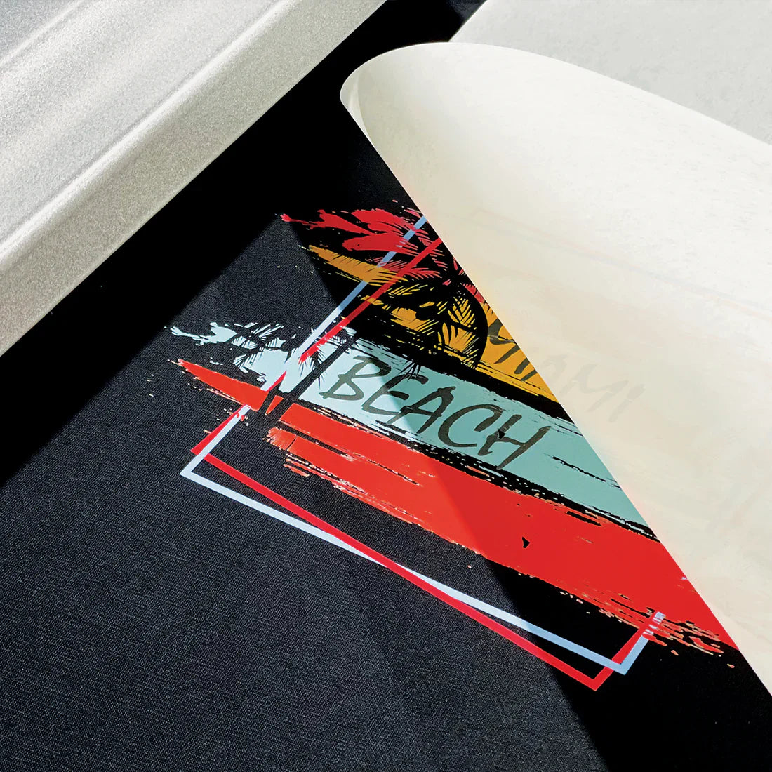 Custom DTF (Direct to Film) heat transfer sheet being peeled off a black fabric, revealing a colorful Miami Beach graphic design with vivid colors and clean lines