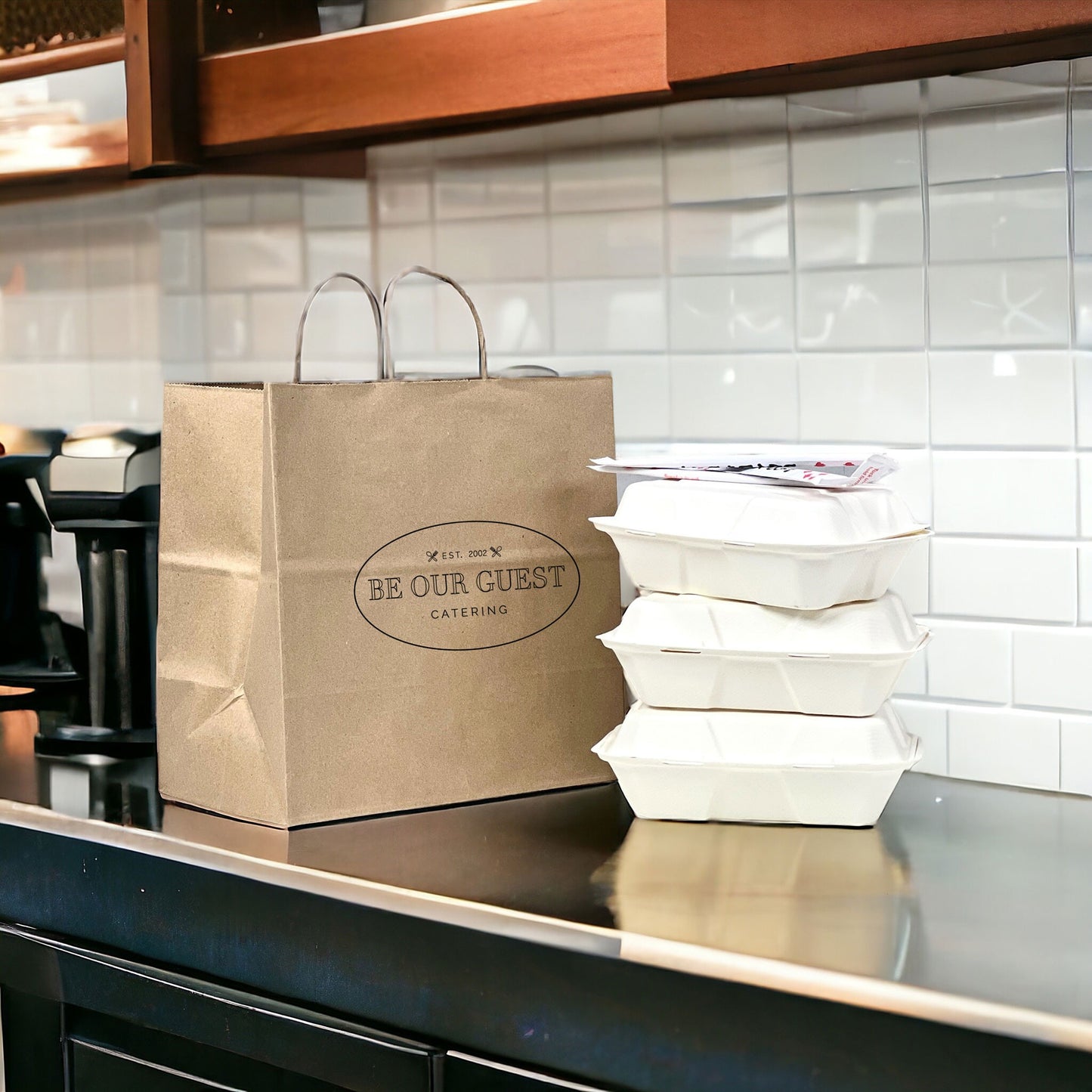 Brown paper bag with 'Be Our Guest Catering' on a kitchen counter with white containers.