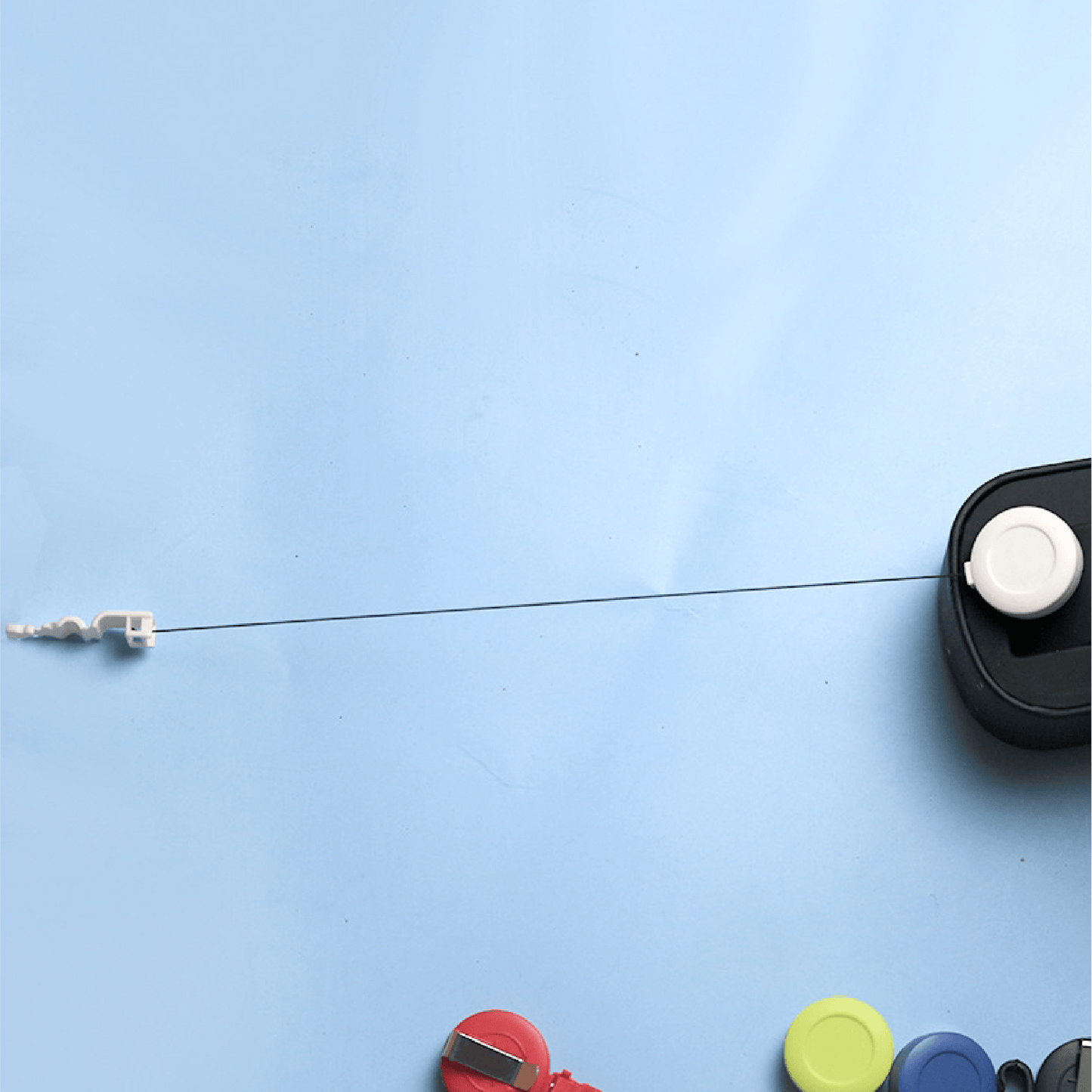Retractable badge reel with extended cord and plastic clip, shown with assorted colorful badge reels on blue background
