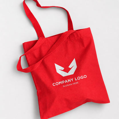 A red canvas tote bag with two shoulder straps, featuring a white geometric logo and the placeholder text 'COMPANY LOGO' and 'SLOGAN HERE' printed on the front, set against a light gray background.